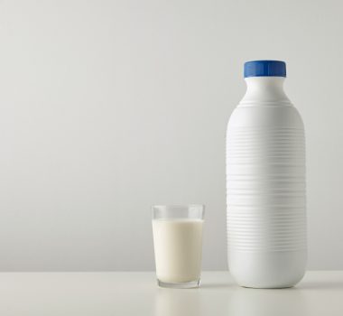 Transparent glass with fresh organic milk near plastic riffled b Transparent glass with fresh organic milk near plastic riffled blank bottle with blue cap isolated on side of white table Space for your text above Retail set, rich texture