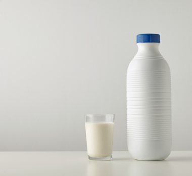 Transparent glass with fresh organic milk near plastic riffled blank bottle with blue cap isolated on side of white table Space for your text above Retail set, rich texture